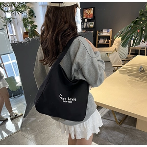 Vue détaillée du sac cabas en toile noire avec lettrage blanc porté par un modèle