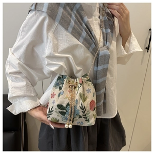 Close-up of floral jacquard bucket bag featuring white pearl drawstring and chain strap