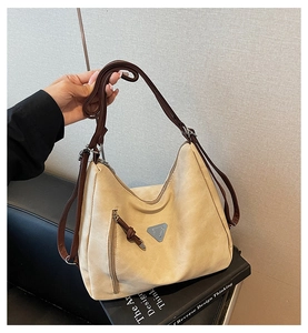 Close-up of beige tote bag with brown leather strap and triangle logo on books
