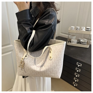 Detail of monogram tote bag with beige logo pattern and gold letter R metal charm