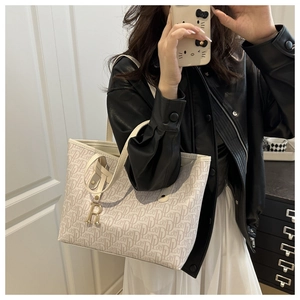 Detail of cream tote bag with vintage monogram pattern and golden R-shaped charm