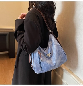 Gros plan du sac porté épaule en jean bleu avec logo triangle en métal et poche zippée