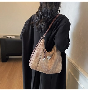 Détail du sac à bandoulière en daim marron avec logo triangle et pompons décoratifs