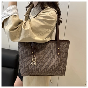 Detailed close-up of brown monogram tote bag with gold R charm and metal rivets