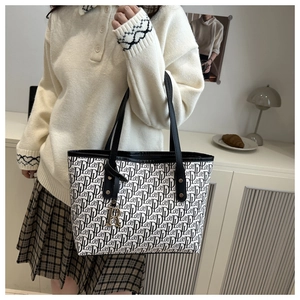 Close-up of printed canvas tote bag with leather straps and golden letter charm detail
