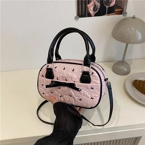 Pink bowling handbag with black bow decoration and crossbody strap shown on a table