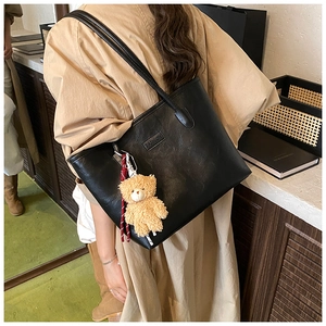 Detail of black tote bag with plush bear charm worn by a model in a cozy indoor setting
