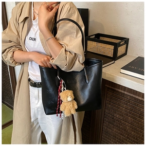 Close-up of black leather tote bag with embossed fashion text and plush bear charm