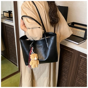 Close-up of black leather tote bag with FASHION label and cute brown plush bear charm