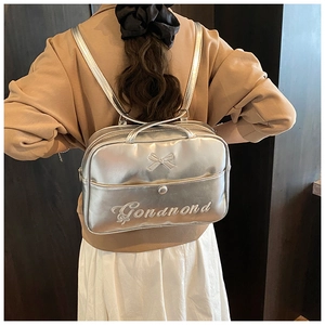 Silver glossy backpack with bow decoration and embroidery shown on model back