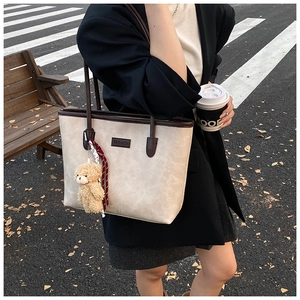 Detail of minimalist cream tote bag with brown handles and a cute plush bear charm