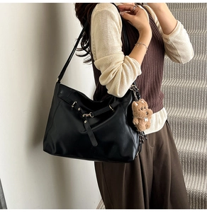 Detail of a black glossy leather tote bag with a brown plush bear charm accessory