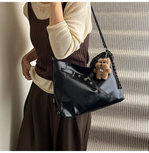 Detail of black glossy faux leather tote bag with decorative straps and a plush bear charm