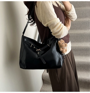 Detail of black faux leather tote backpack with a brown bear plush charm on a model