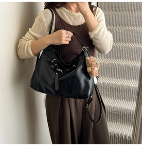 Detail of a black leather crescent hobo bag with a brown teddy bear charm on shoulder