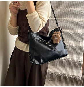 Detail of black leather tote bag with decorative buckle and plush bear charm pendant