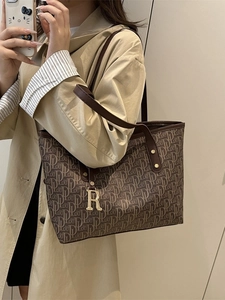 Retro brown monogram tote bag with leather handles and gold charm shown on a model