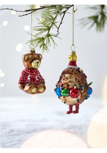 Detail of Christmas bear and hedgehog glass ornaments hanging on snowy pine branches