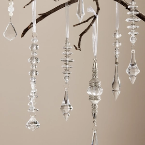 Elegantes carámbanos de acrílico y cuentas de cristal colgados en ramas con lazos blancos
