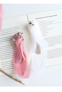 Close-up of pink glitter and white feather decorative birds on a vintage open cookbook