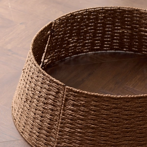 Brown woven Christmas tree collar with textured wicker pattern on dark wooden floor