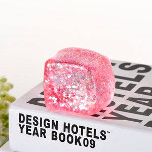 Detail view of a translucent pink glitter squeeze toy cube on a white decorative book