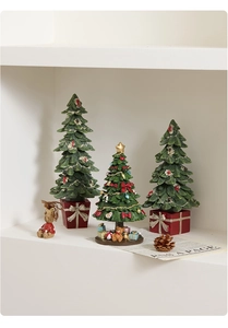 Close-up of three decorative resin Christmas trees with festive ornaments and red bases