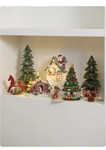 Illuminated resin Christmas house and miniature tree ornaments on a cozy shelf