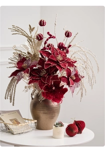 Close-up of velvet red poinsettia with gold glitter branches in a bronze ceramic vase