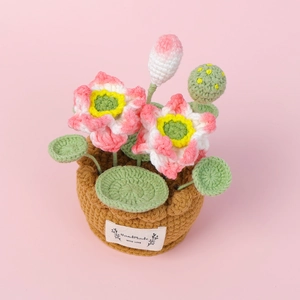 Handmade crochet lotus potted plant with pink flowers and green leaves on pink background