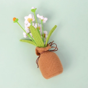 Handmade crochet white daisy potted plant with green leaves in a brown woven base