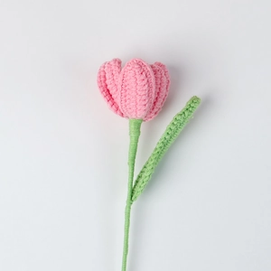 Detail of a handmade pink crochet tulip flower with green stem and knitted leaf