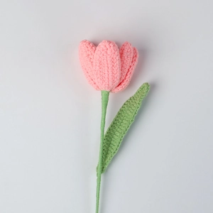 Close-up of handmade pink knitted tulip flower with soft yarn texture and green stem