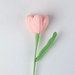Close-up of handmade pink crochet tulip with fine knitted texture and green leaf detail