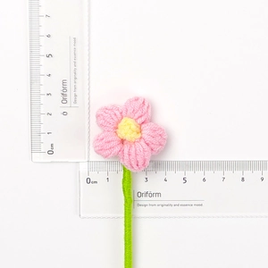 Dettaglio di un piccolo fiore all'uncinetto rosa da 3cm fatto a mano con stelo verde