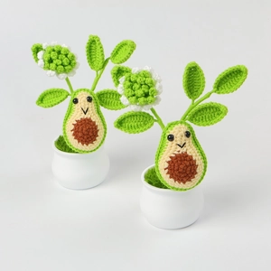 Detail of two handmade crochet avocado plants with cute faces in white ceramic pots