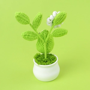 Handmade crochet potted plant with cute bird design in a white ceramic pot on green background