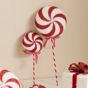 Red and white glitter candy cane Christmas tree picks with bow ornaments on beige background