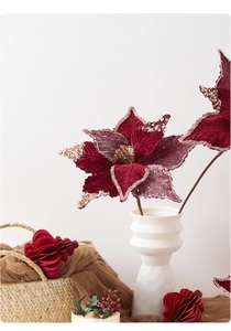 Detailed view of burgundy velvet poinsettia with gold glitter in white ceramic vase