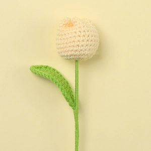 Close-up of handmade crochet tulip in beige yarn with green leaves on soft yellow background