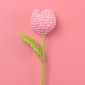 Detail of pink hand-knitted tulip flower with soft yarn texture and green leaf
