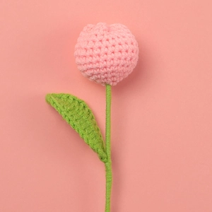 Macro shot of handmade crochet tulip with pink yarn petals and green knit leaf