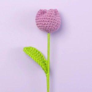 Close-up of handmade crochet tulip with purple yarn texture and green knitted leaves