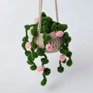 Detail of handmade crochet hanging plant with pink flowers and green vines on beige pot