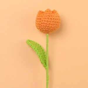 Close-up of a hand-knitted orange tulip with green leaves made from premium cotton yarn