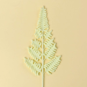 Close-up of hand-knitted green fern leaf branch with detailed crochet yarn texture