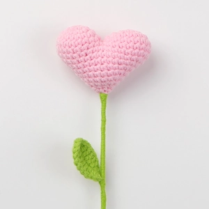 Detailed view of hand-crocheted pink heart flower with green stem and leaf textures