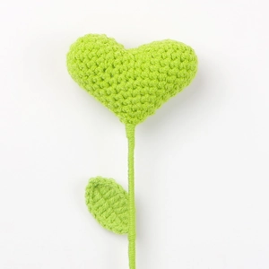 Macro shot showing detailed hand-knitted green heart flower with crochet texture