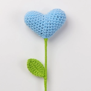 Macro detail of a hand-knitted blue heart flower with crochet texture and green stem