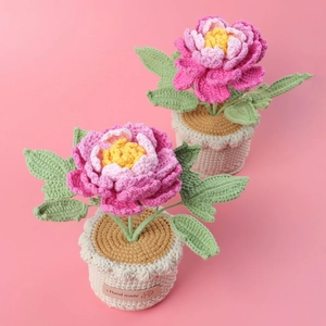 Detail of handmade crochet peony potted plant with leather 'Hand made' label on pink backdrop